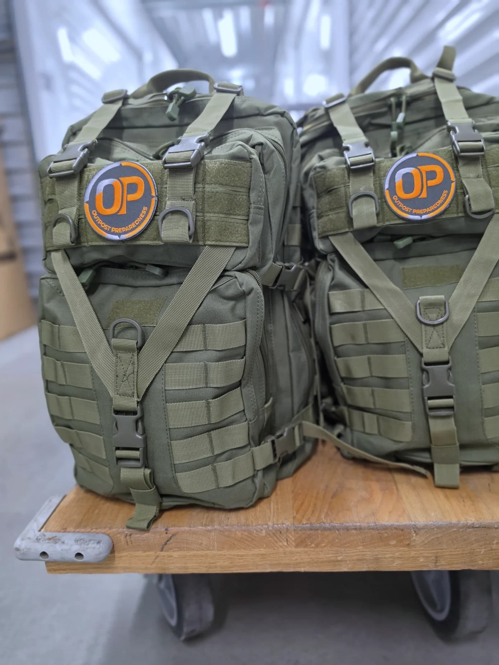 Two packed Outpost Essential+ Go-Bags on a warehouse cart, OP patches forward