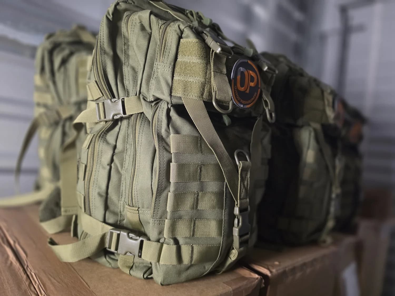 A row of packed Outpost go-bags lined up on a bench, patches forward, ready to be picked up